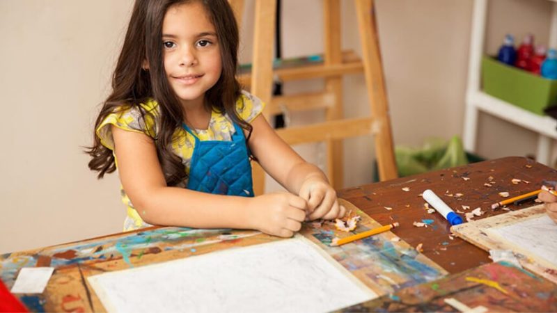 A child in an apron drawing and crafting at a classroom table